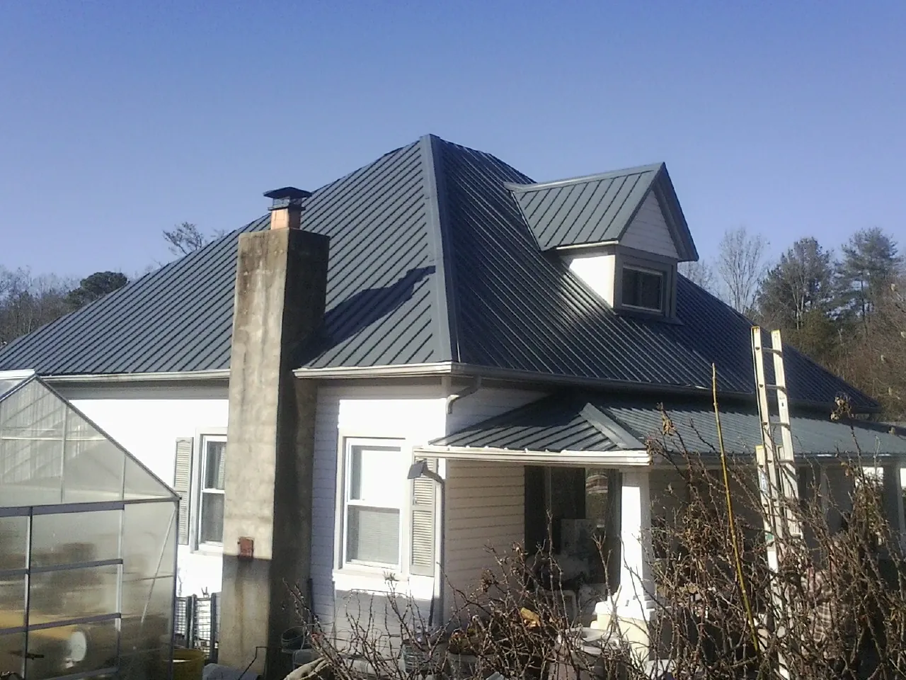 Dark blue standing seam metal roof on a white farmhouse with dormer — Slate & Tile Roof Repair by Roofing Brothers in Mohrsville