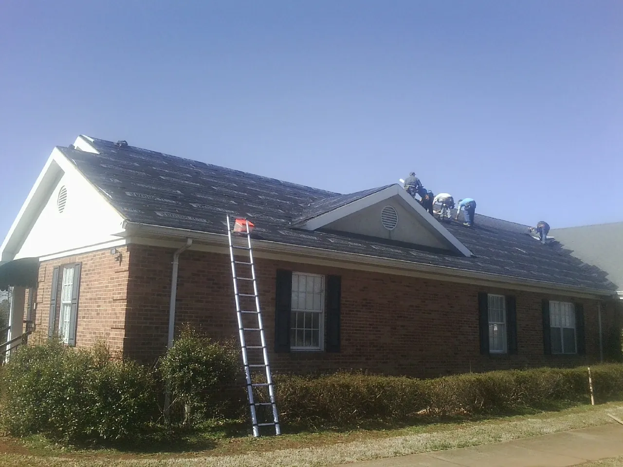 Crew tearing shingles off a brick ranch roof with a ladder set — Metal Roof Repair work by our crew in Mohrsville