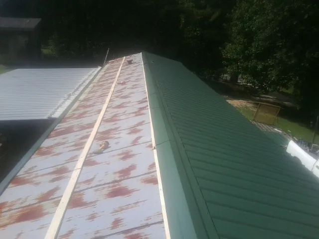 Old rusted panels beside newly installed green metal roofing — Wind Damage Roof Repair by Roofing Brothers in Mohrsville