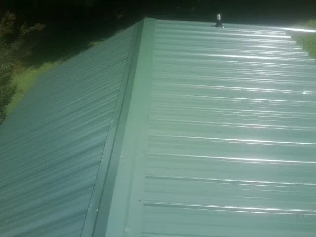 New green metal panels meeting at the ridge of a roof — Flat Roof Repair work by our crew in Mohrsville