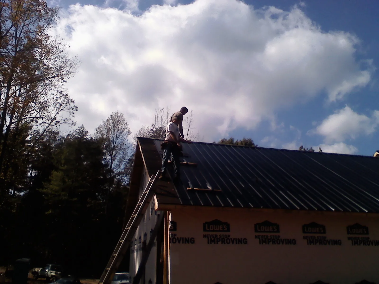 Roofer fastening dark metal panels high against a cloudy sky, from a Roof Inspection job in Mohrsville
