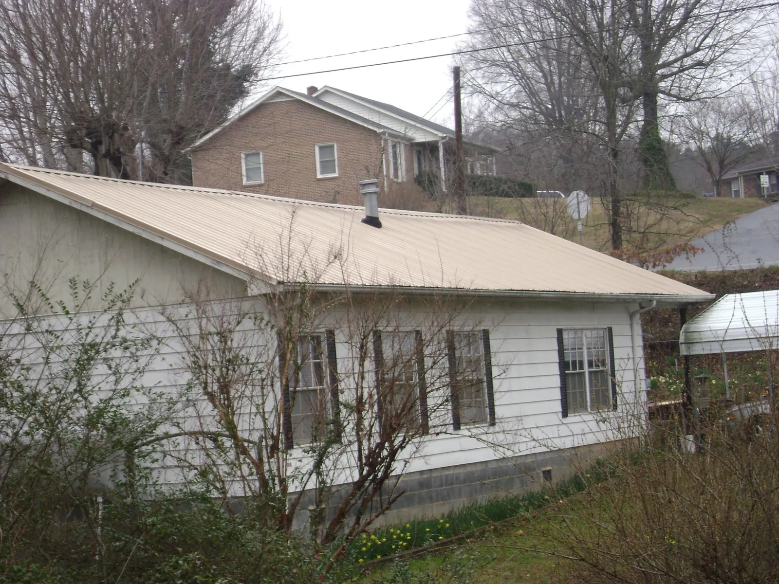 Tan metal roof on a white sided house set into a hillside — Commercial Roofing by Roofing Brothers in Mohrsville